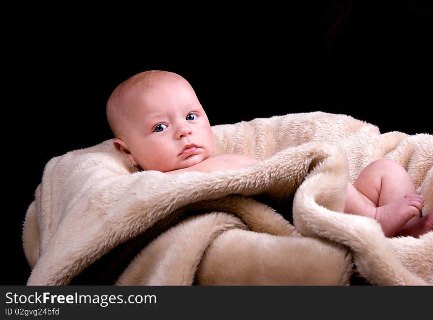 3 Month old baby lying naked on a fluffy blanket on a black background