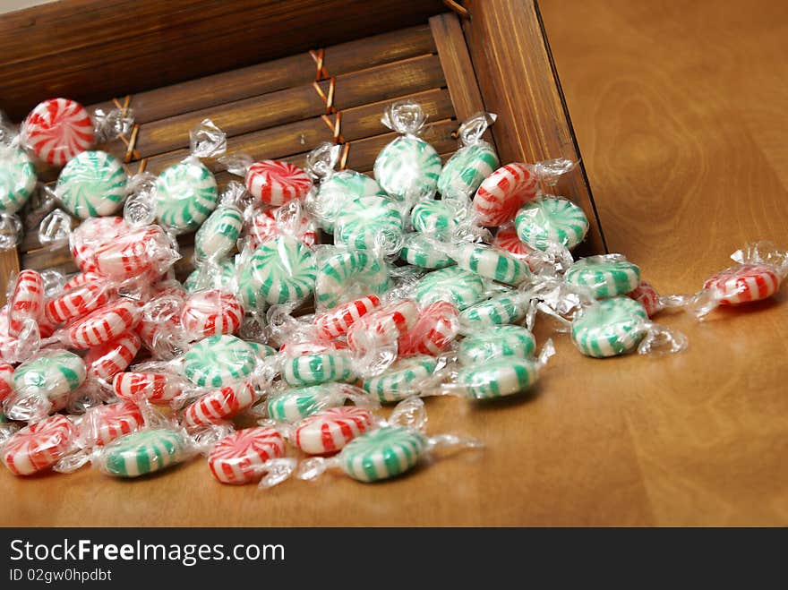 A closeup of peppermint swirl candies spilling from a wooden container. A closeup of peppermint swirl candies spilling from a wooden container.