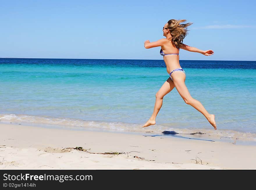 Charming tanned girl running across a sandy beach along the ocean