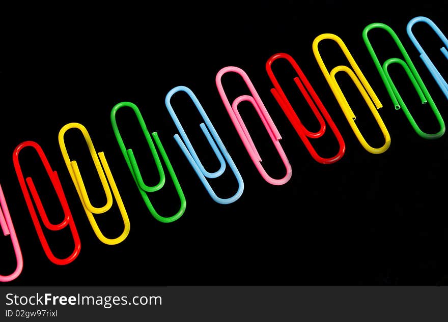 Bunch of paper clips on black background. Loose paper clips in background.