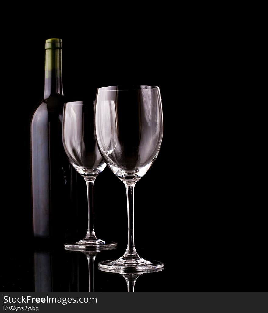 Bottle of red wine and empty glasses wrapped in a dark ambiance of a cellar with black background. Bottle of red wine and empty glasses wrapped in a dark ambiance of a cellar with black background