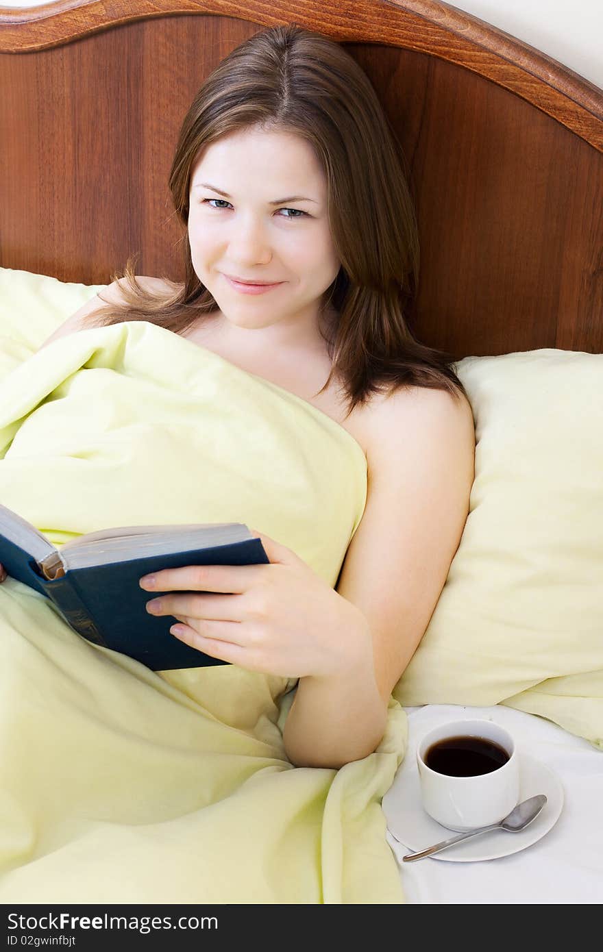 Young beautiful woman with book and cup of coffee in the bed. Young beautiful woman with book and cup of coffee in the bed