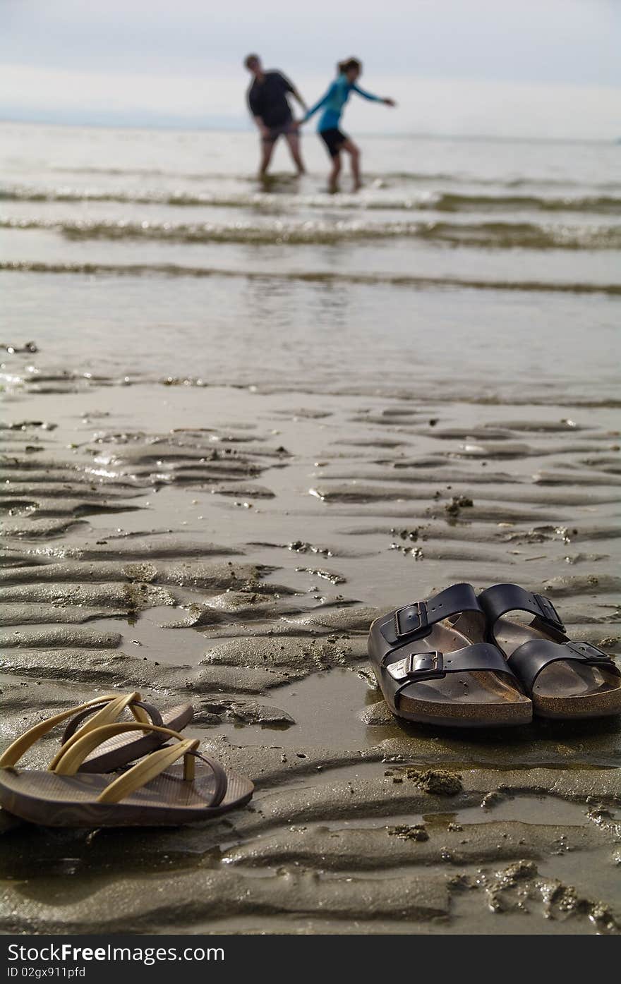 A couple who ran to the beach left their sandles on the beach to play in the water. A couple who ran to the beach left their sandles on the beach to play in the water