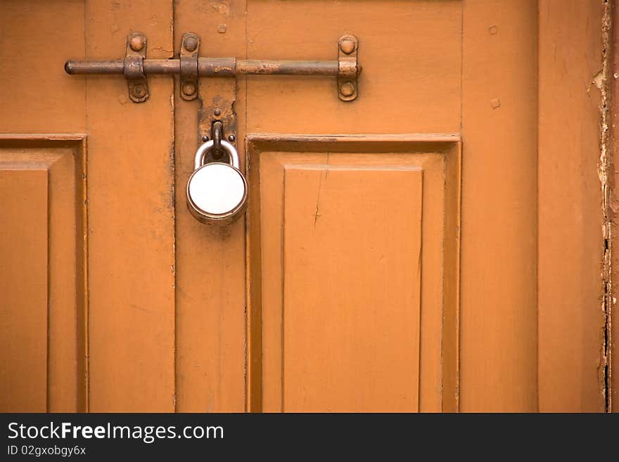 Locked dark orange door of a very old house seems quite durable and strong. Locked dark orange door of a very old house seems quite durable and strong