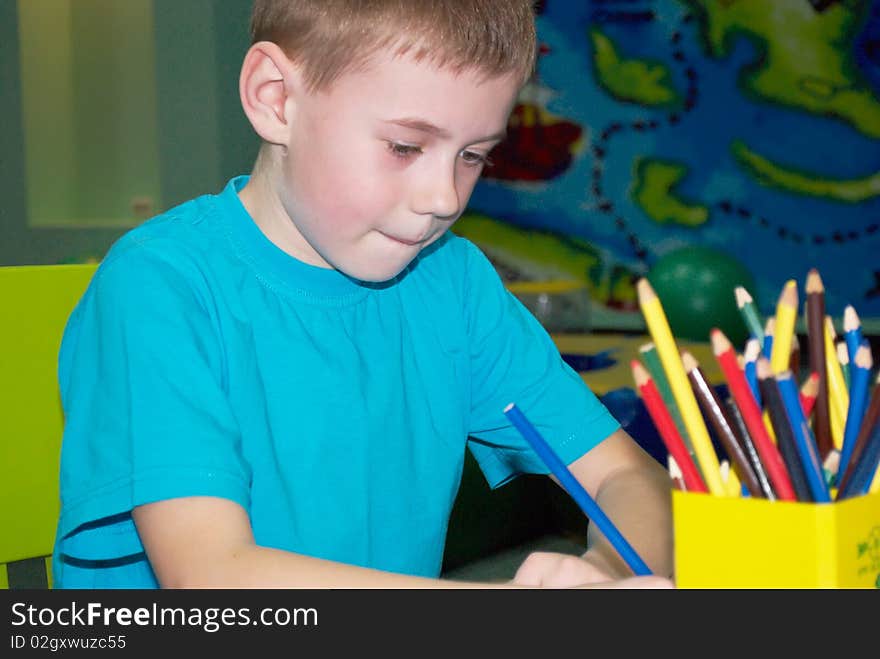 The boy draws something sitting on a table. The boy draws something sitting on a table