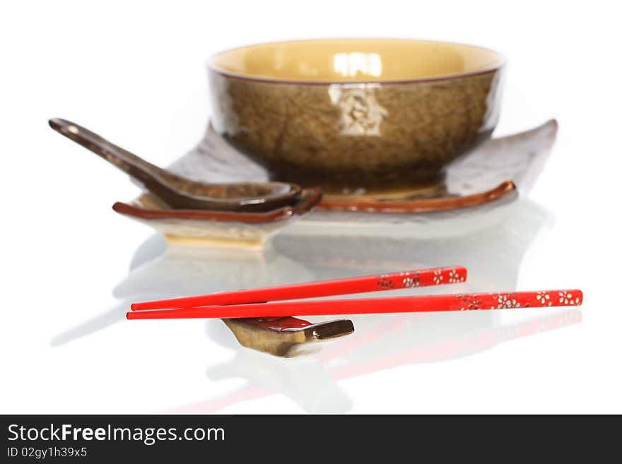 Pair of red chopsticks on white background with set of ceramic japanese dishware