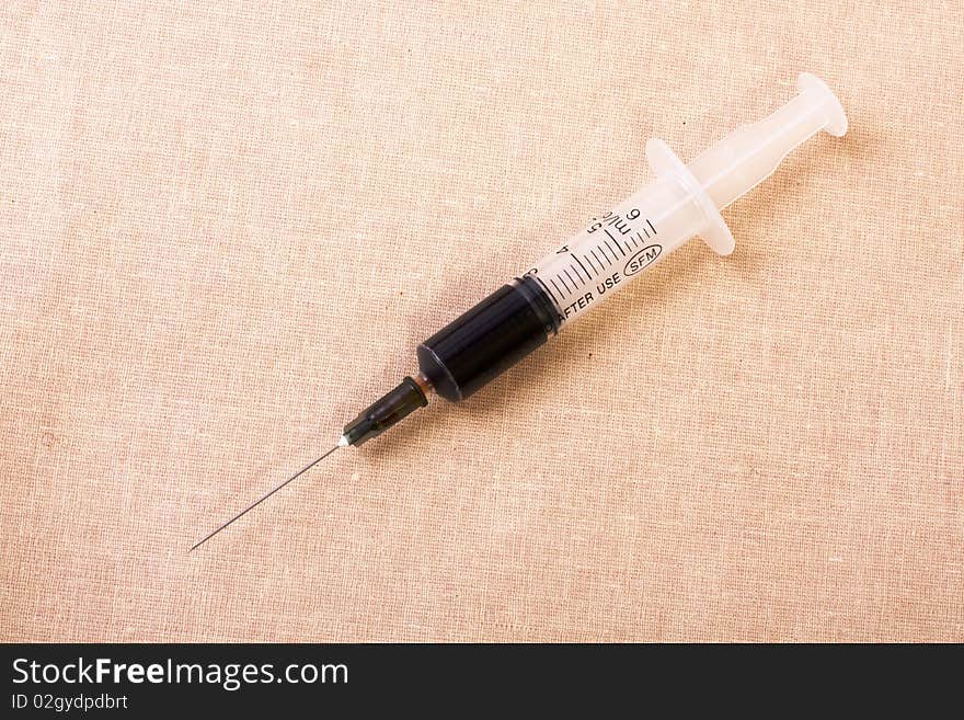 Syringe with brown vaccine on the canvas. Syringe with brown vaccine on the canvas