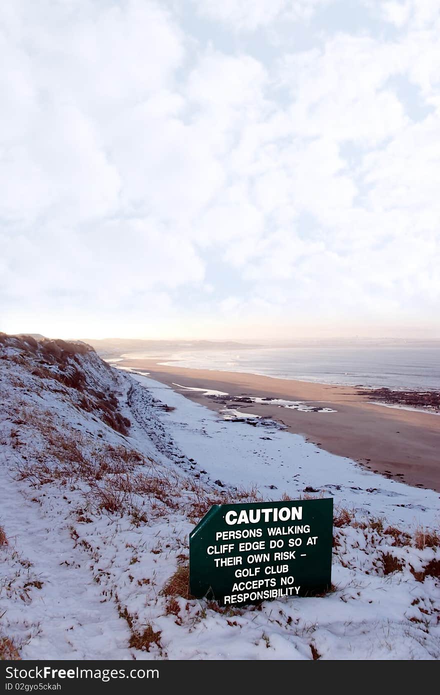 A caution sign on a cliff edge in snow covered ballybunion. A caution sign on a cliff edge in snow covered ballybunion