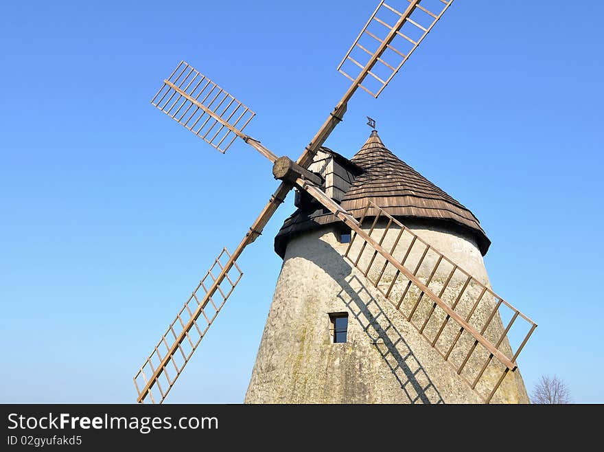 A windmill is a machine which converts the energy of wind to rotational motion by means of adjustable vanes called sails. The main use is for a grinding mill powered by the wind, reducing a solid or coarse substance into pulp or minute grains. A windmill is a machine which converts the energy of wind to rotational motion by means of adjustable vanes called sails. The main use is for a grinding mill powered by the wind, reducing a solid or coarse substance into pulp or minute grains.