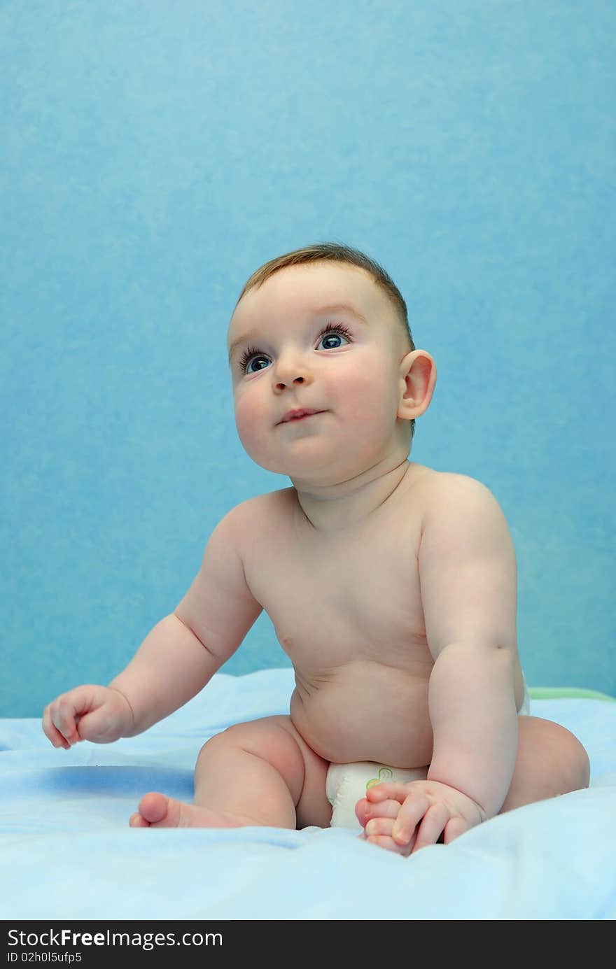 The happy baby sits in diapers and looks upwards. The happy baby sits in diapers and looks upwards