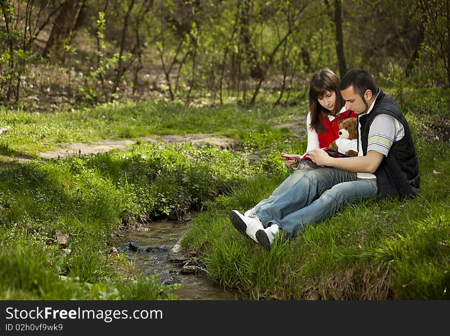 Girl and boy sitting and reading near a river. Girl and boy sitting and reading near a river