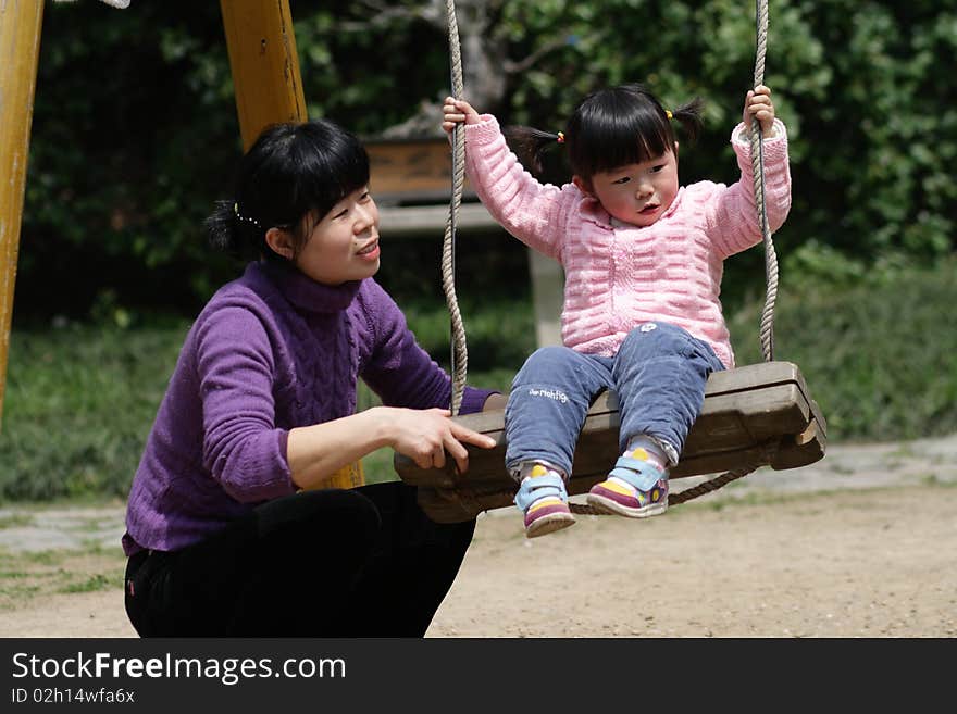 He girl is playing on the swing，her mother looking after her carefully. He girl is playing on the swing，her mother looking after her carefully