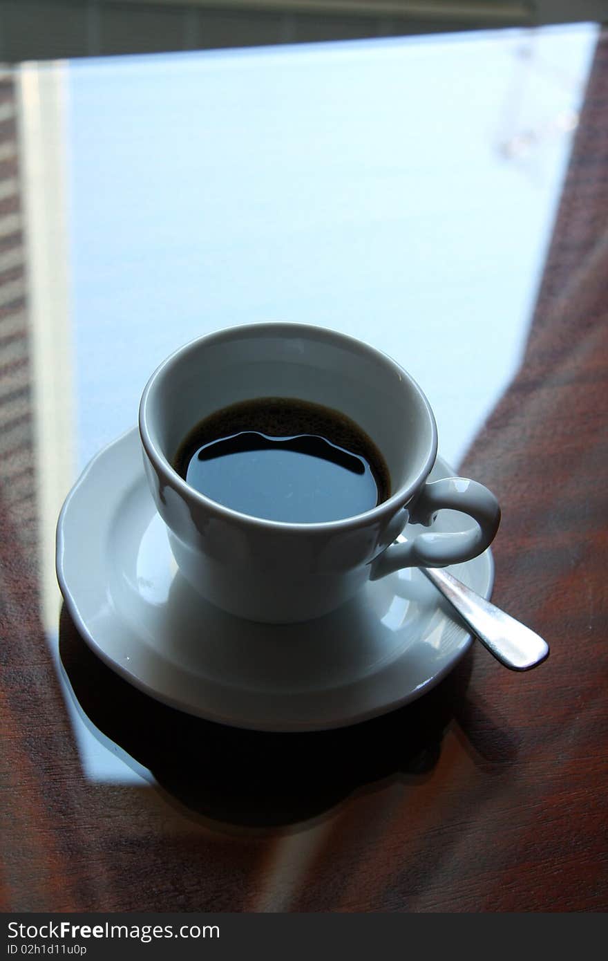 Close up view of a coffee  cup on a wood and crystal table under a window. Close up view of a coffee  cup on a wood and crystal table under a window