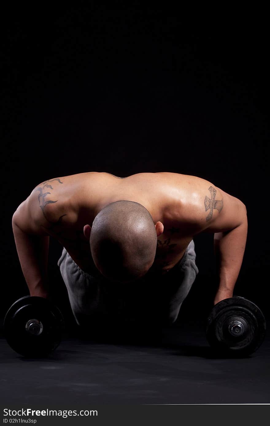 Young bald strong man is working out over black background. Young bald strong man is working out over black background.