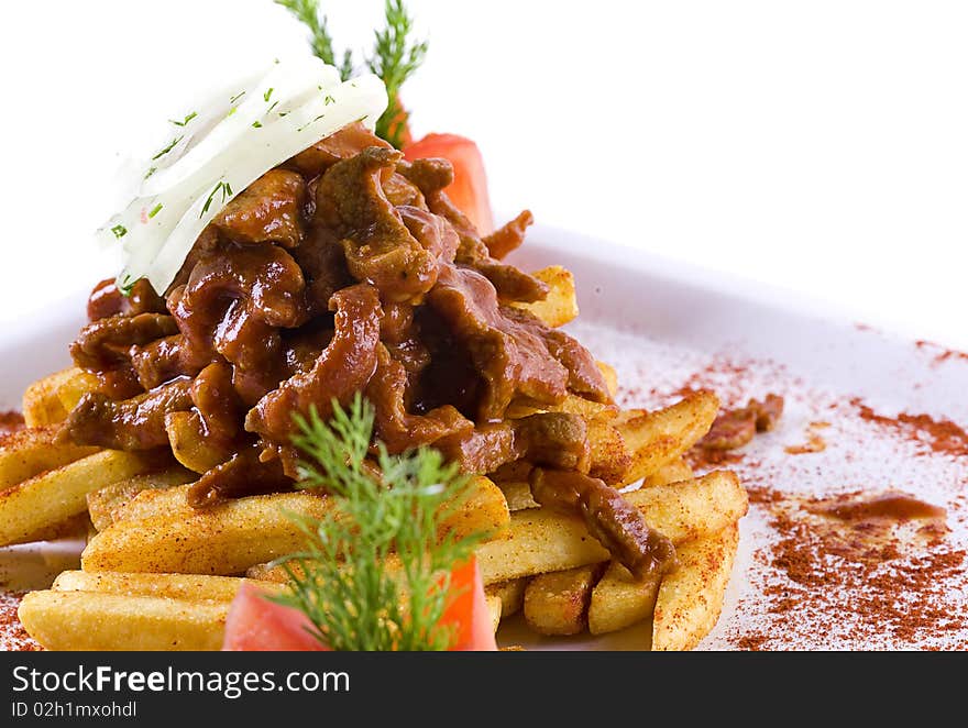 Meat with fries decorated with tomatoes and onion on white plate