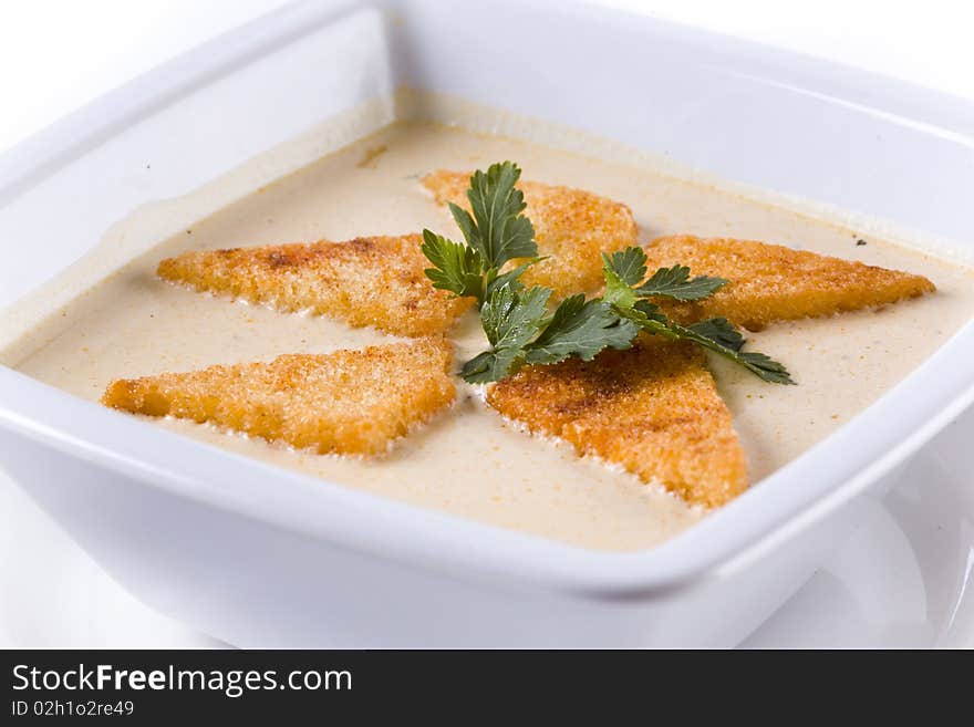 A bowl of cream soup, garnished with parsley and toast. close up