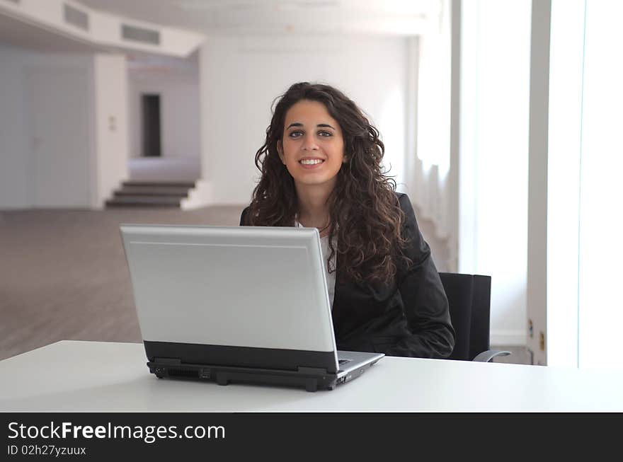 Portrait of a young smiling businesswoman sitting at the office in front of a laptop. Portrait of a young smiling businesswoman sitting at the office in front of a laptop