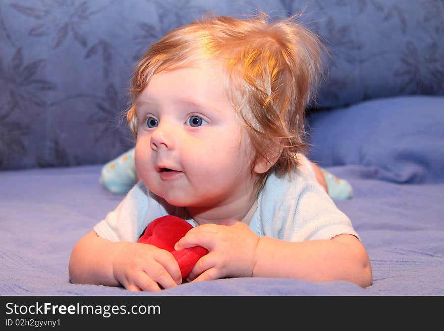 Nice blue-eyed baby playing with red toy on blue sofa. Nice blue-eyed baby playing with red toy on blue sofa