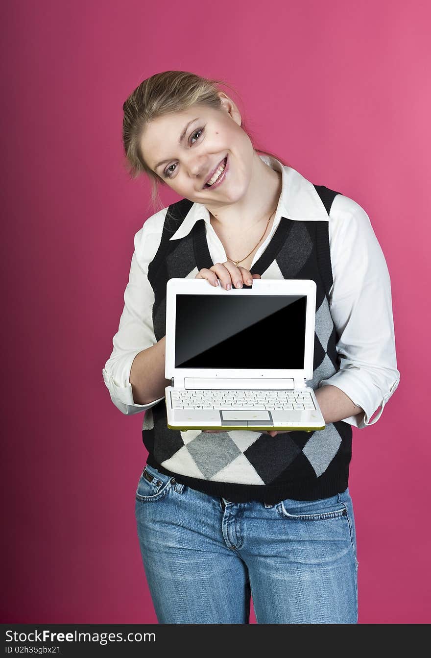 Blond young woman with laptop posing on pink background, studio shot