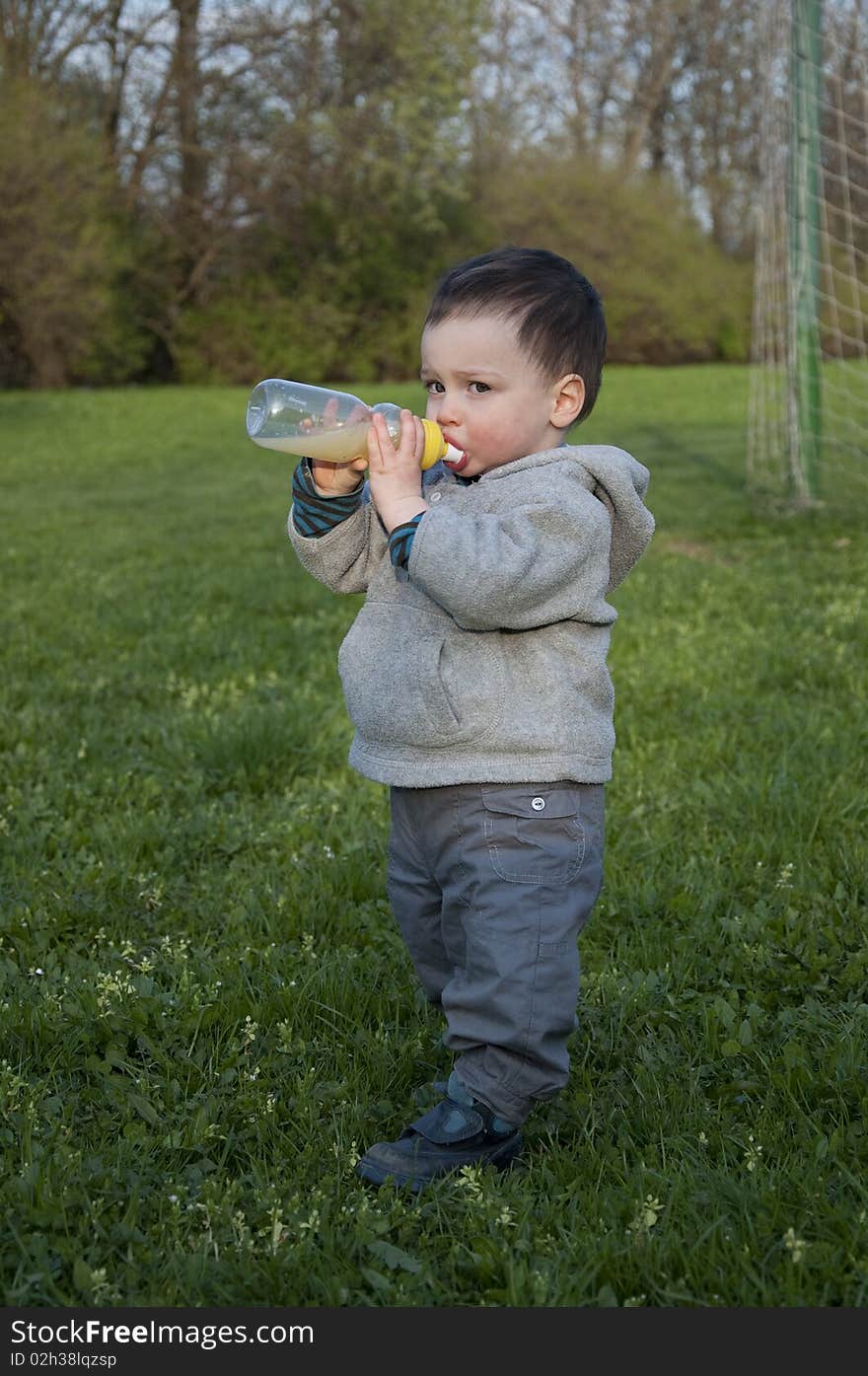 A toddler standing on a grassy field drinking from a plastic bottle. A toddler standing on a grassy field drinking from a plastic bottle.