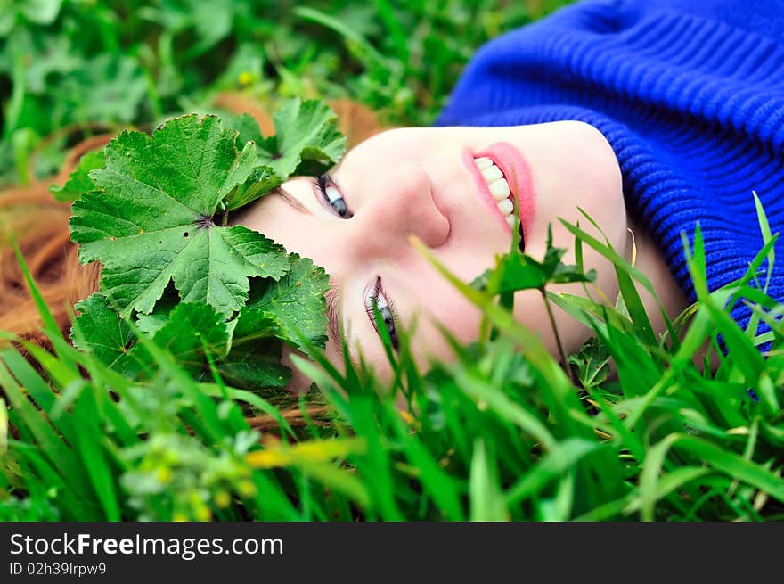 Face of redheaded girl laying on the green grass with crown from leaves