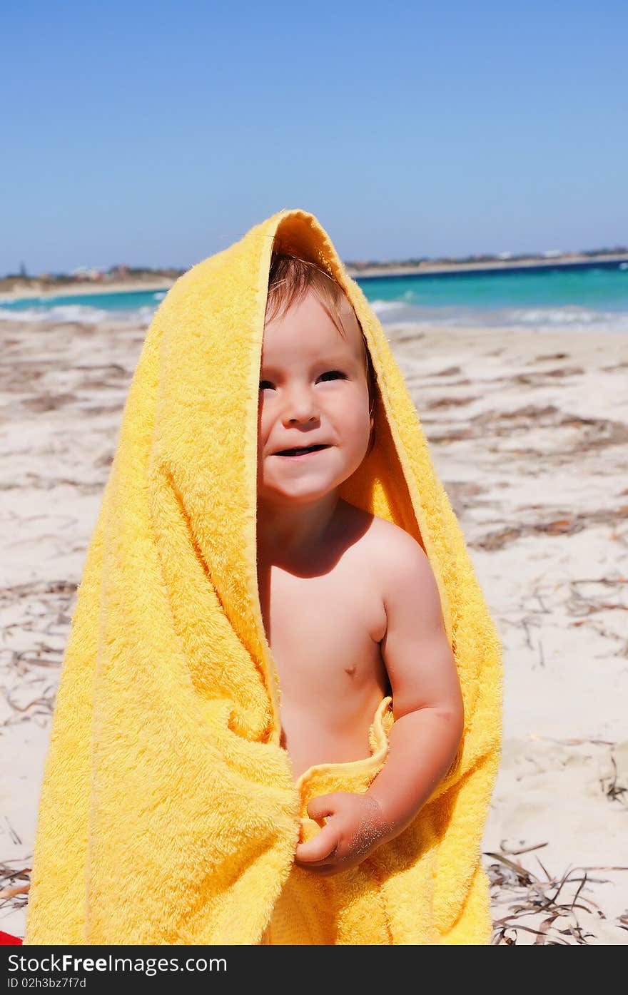 Charming little girl in a yellow towel on the beach as a symbol of childhood happiness and joy