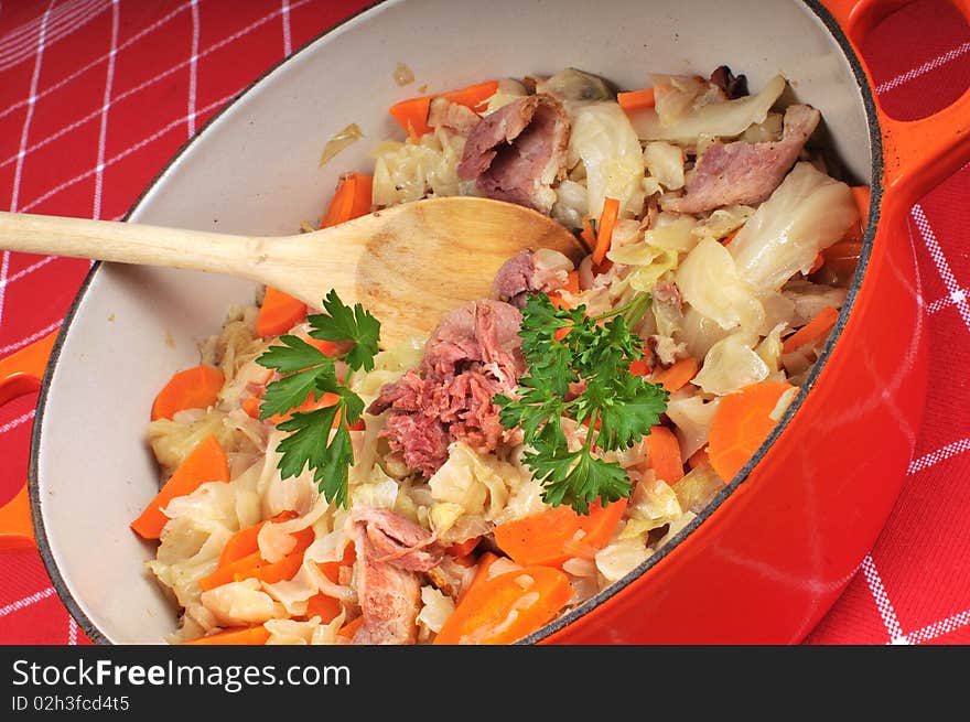 Large pot filled with ham, cabbage and carrots and parsley. The table is dressed with a checkered red cloth. Large pot filled with ham, cabbage and carrots and parsley. The table is dressed with a checkered red cloth.