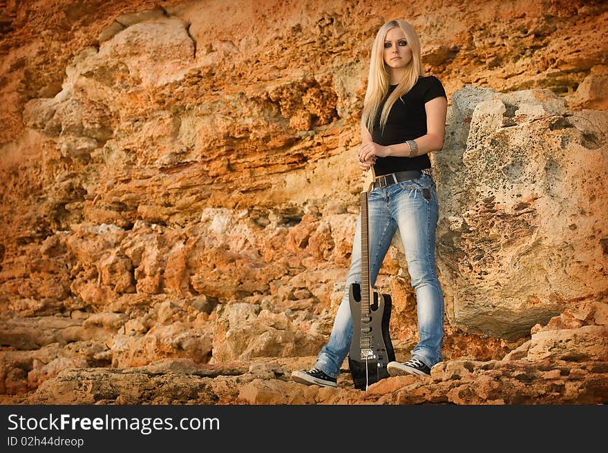 Series. The beautiful blonde with a guitar on rock background