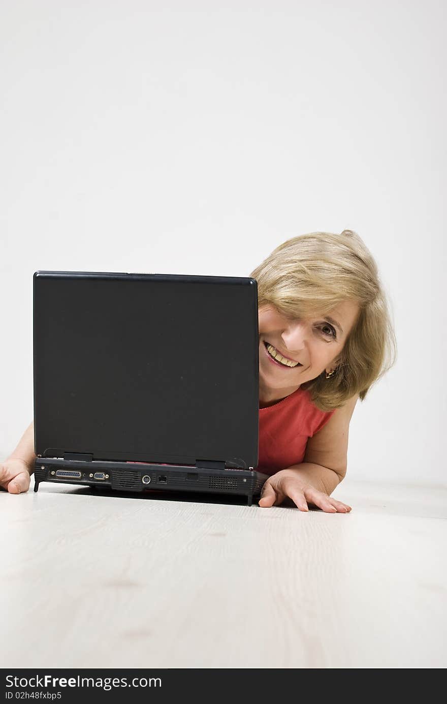 Senior woman laughing and looking behind a laptop while lying down on wooden floor,see more in People on couch or wooden floor. Senior woman laughing and looking behind a laptop while lying down on wooden floor,see more in People on couch or wooden floor