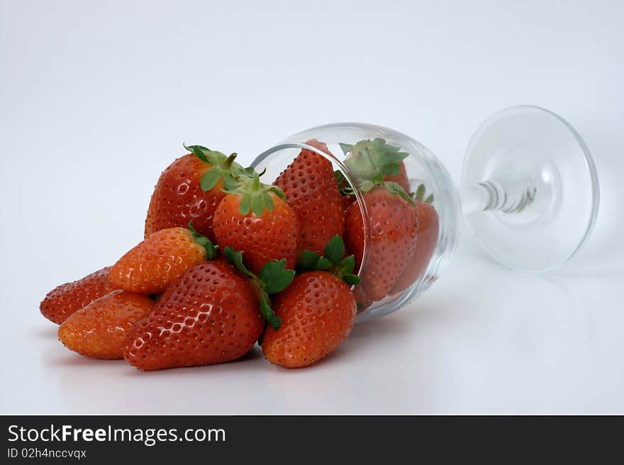 Ripe red strawberries spilling out of an over turned wine glass on a white background. Ripe red strawberries spilling out of an over turned wine glass on a white background.