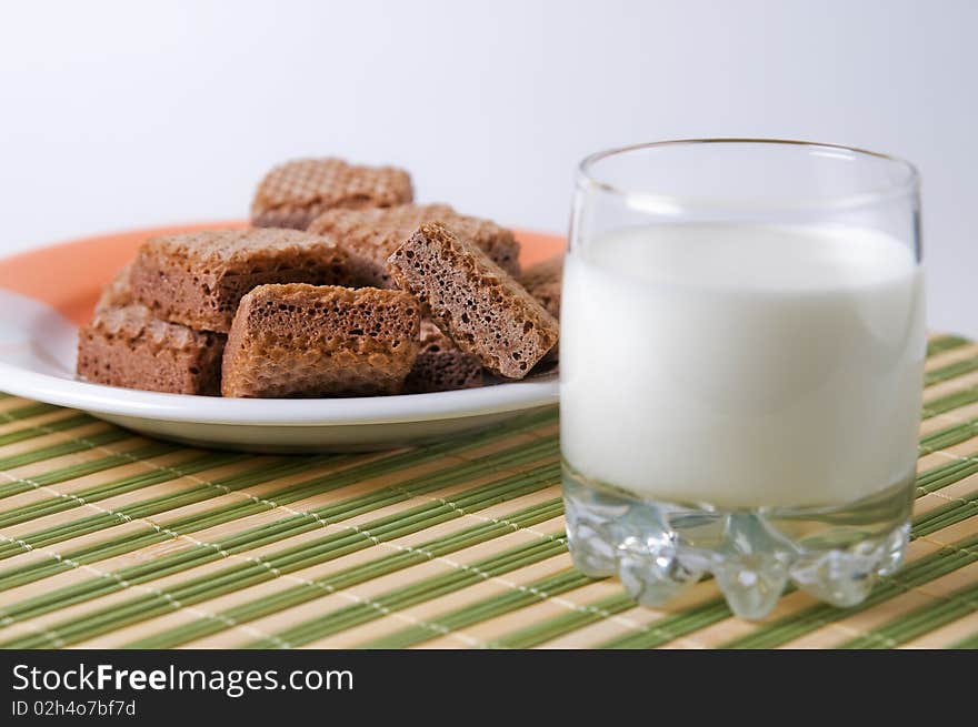 Glass with milk and waffles on plate on stripe surface