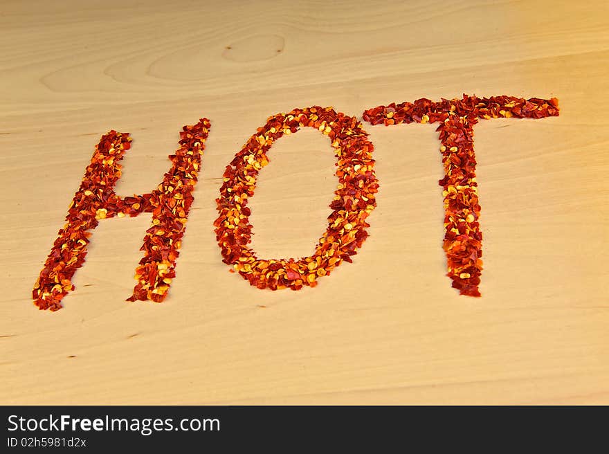 Hot chili flakes, spelled out into the word 'HOT' on a wooden table top.