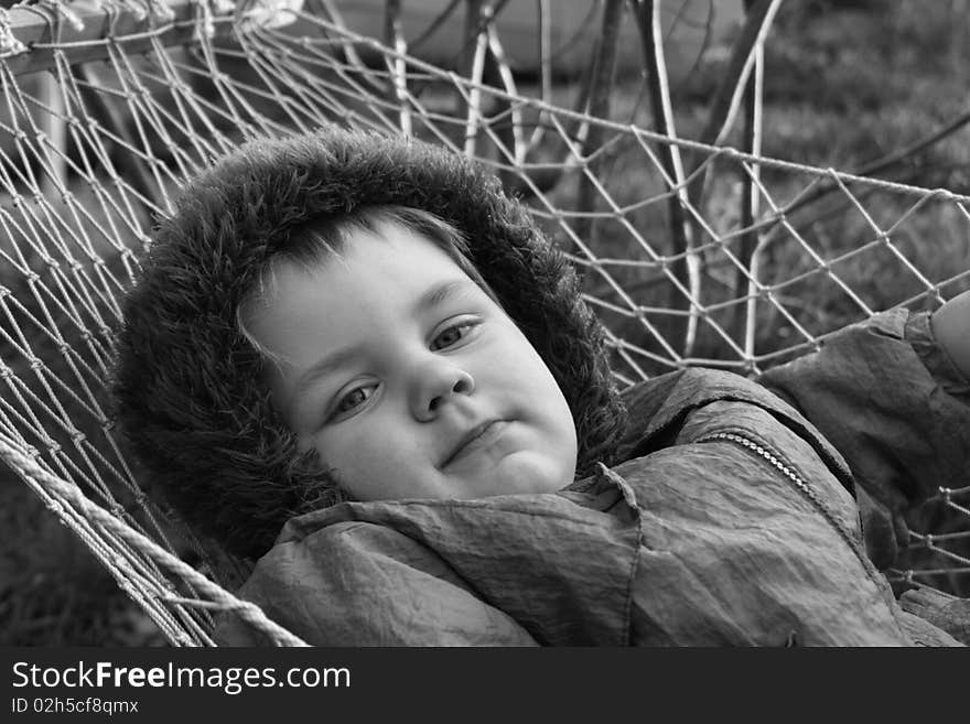 Monochrome portrait of little boy in hammock. He lays quiet and serious looks in the camera. Monochrome portrait of little boy in hammock. He lays quiet and serious looks in the camera