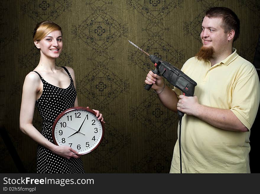 An image of a woman with new clock and a man with drill. An image of a woman with new clock and a man with drill