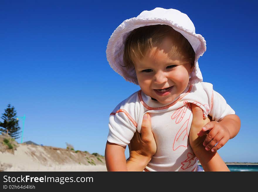 Charming little happy girl laughing in the arms of his mother, against the blue sky