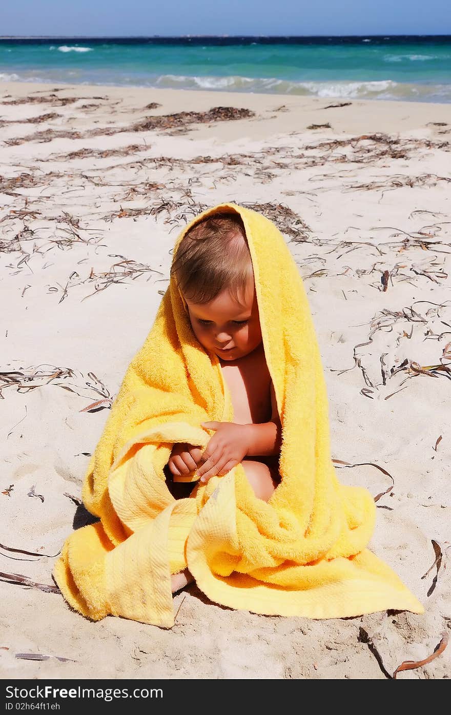 Charming little girl in a yellow towel on the beach as a symbol of childhood happiness and joy