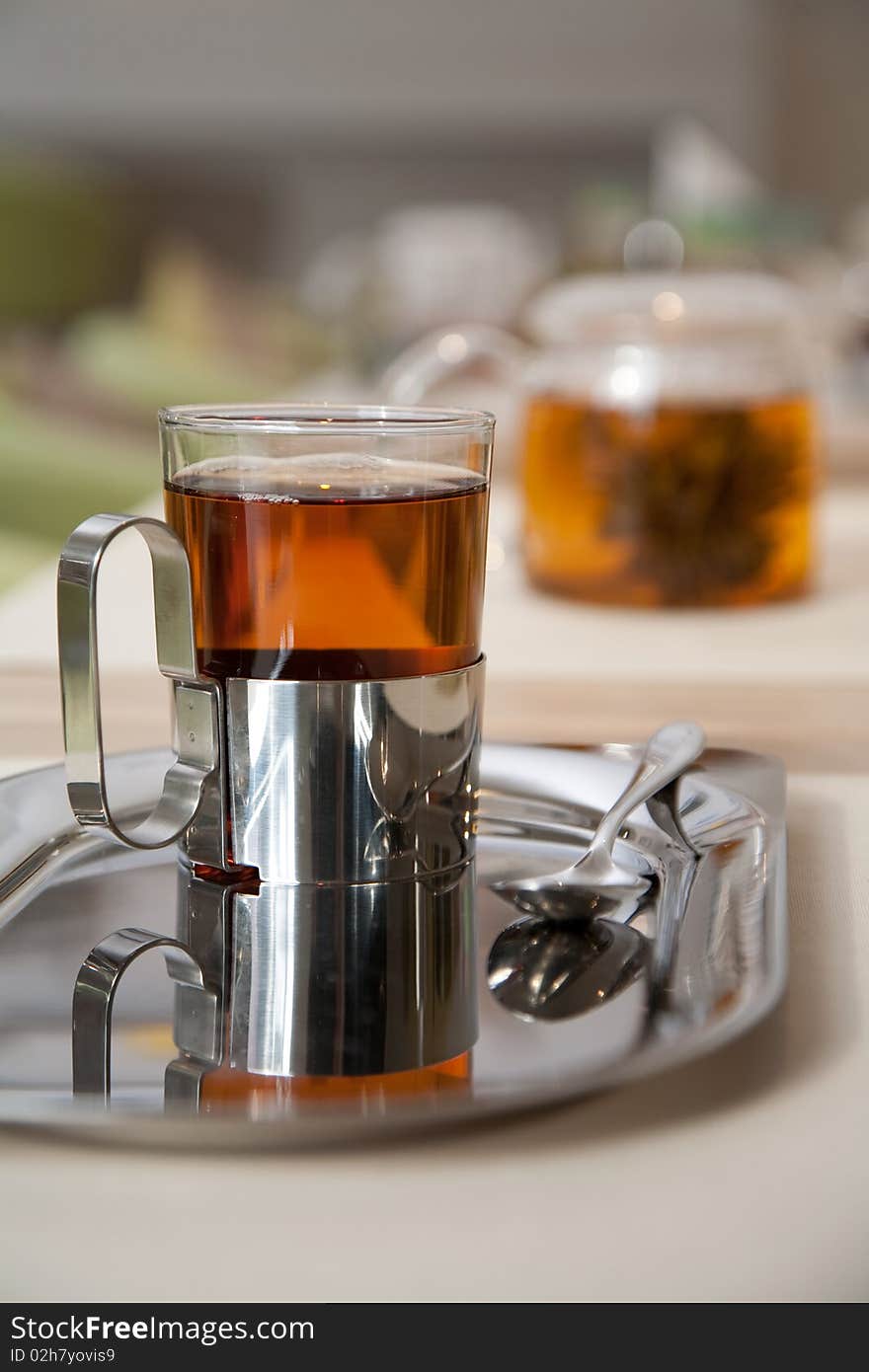 Glass of fresh green tea in a holder standing on an iron tray with a teapot on a background