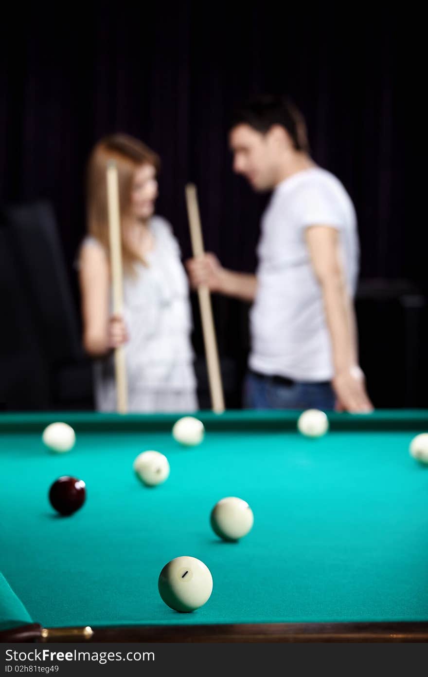 The young couple plays billiards on a back background. The young couple plays billiards on a back background