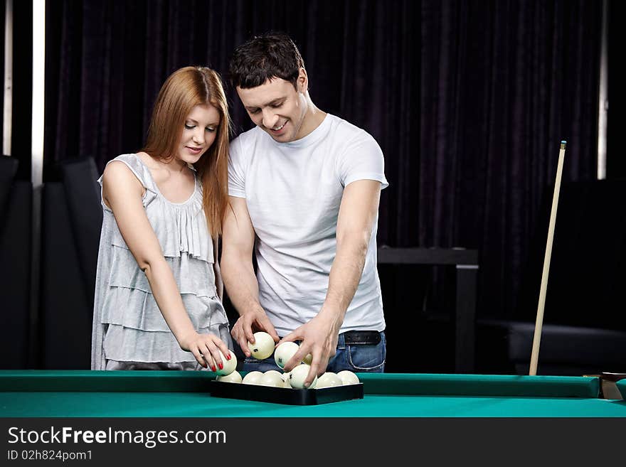 The young couple puts spheres for billiards. The young couple puts spheres for billiards