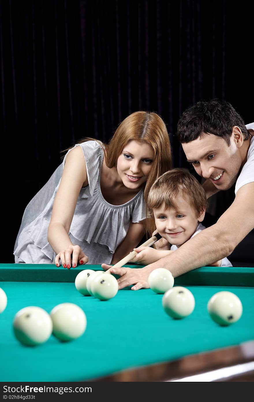 The young couple and the child plays billiards. The young couple and the child plays billiards