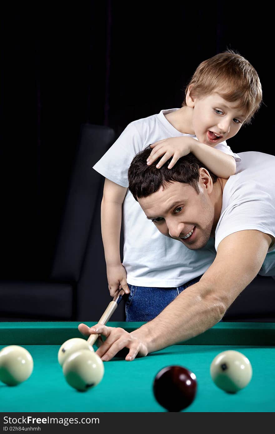 The young man and the little boy play billiards. The young man and the little boy play billiards