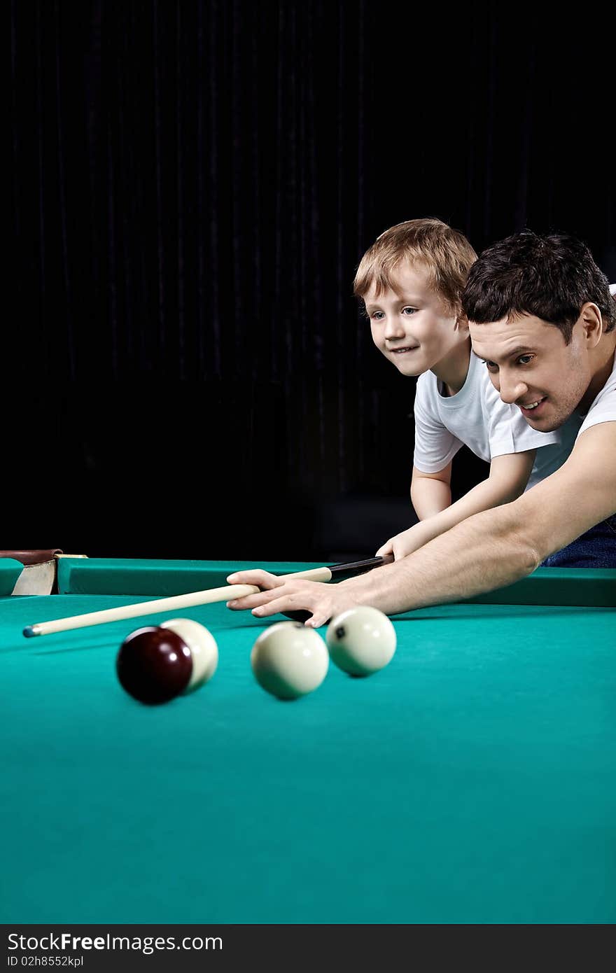 The young man and the little boy play billiards. The young man and the little boy play billiards