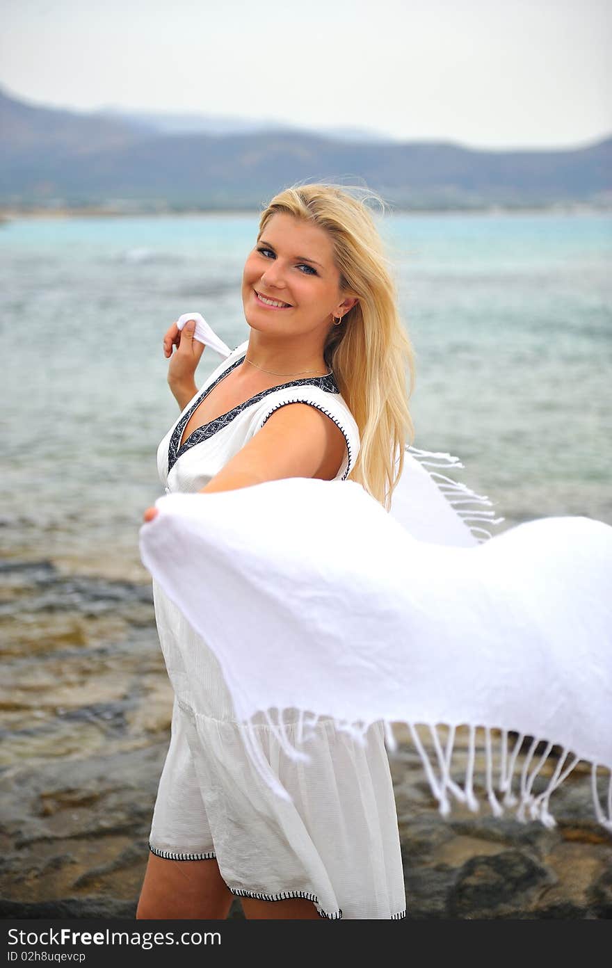 Young beautiful romantic woman in white dress dancing with shawl near blue sea