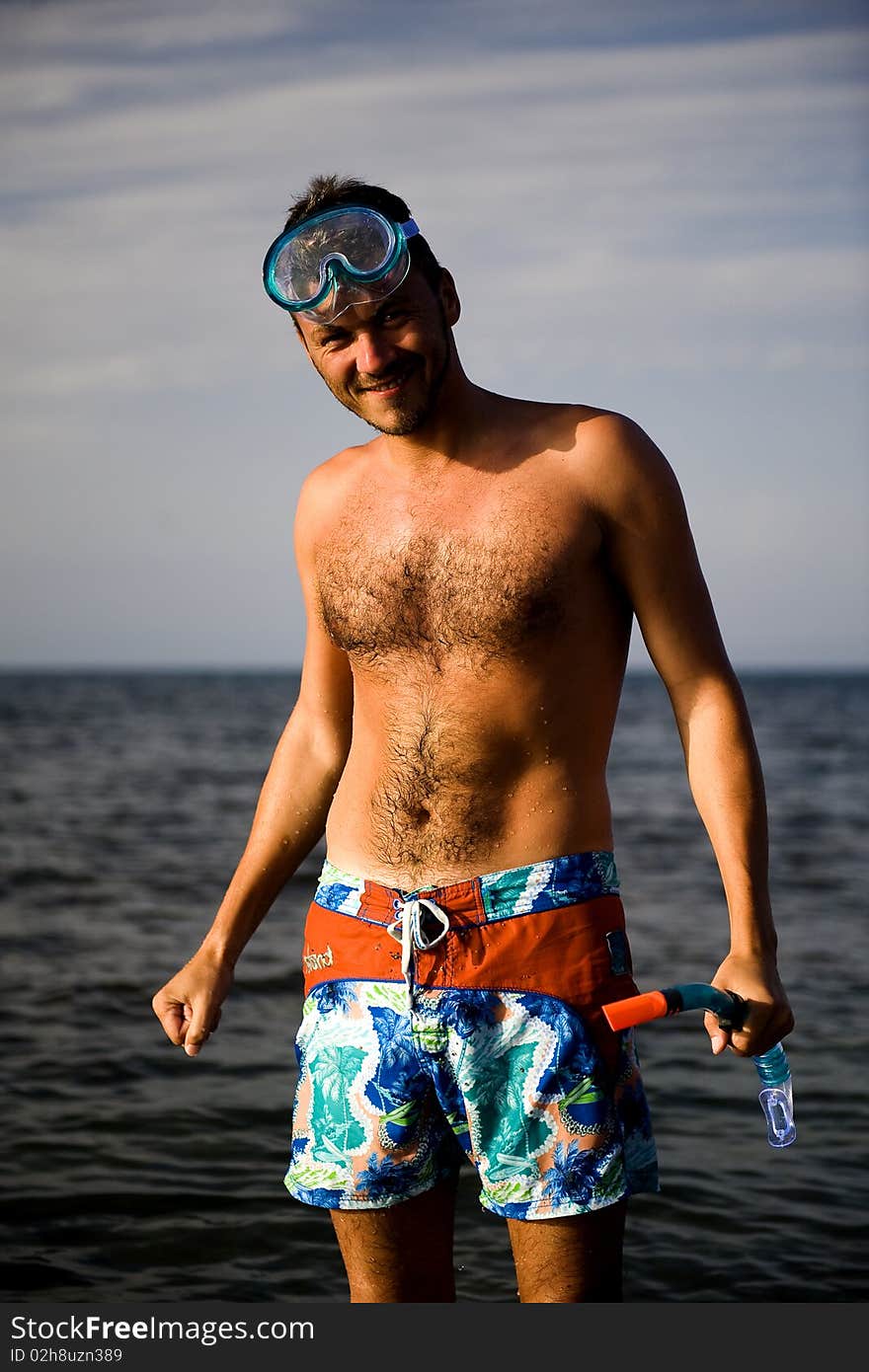 Young happy handsome summer diving man with swimming mask and snorkel preparing to dive in blue sea