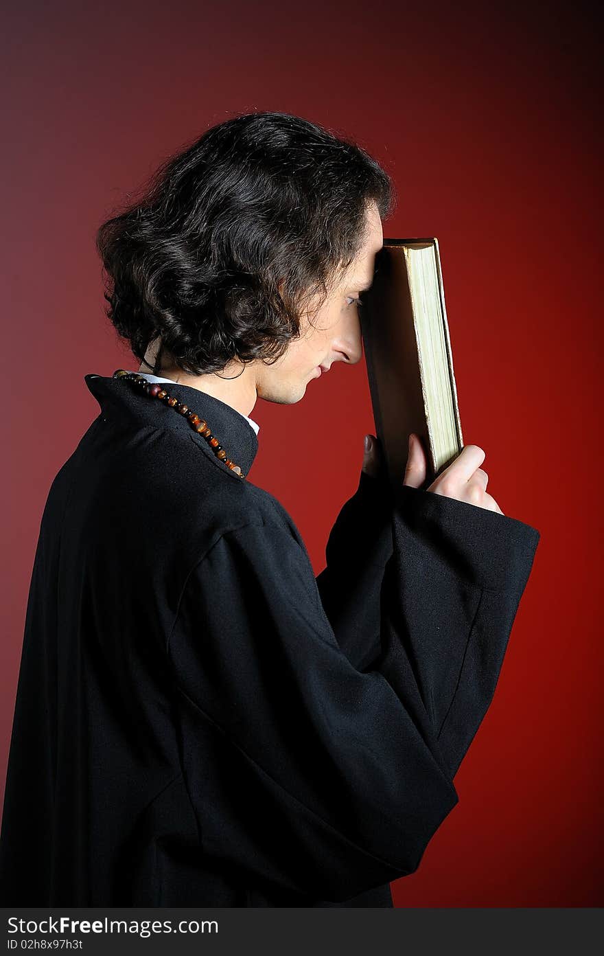 Conceptual portrait of Praying priest with wooden cross and Holy Bible. red background