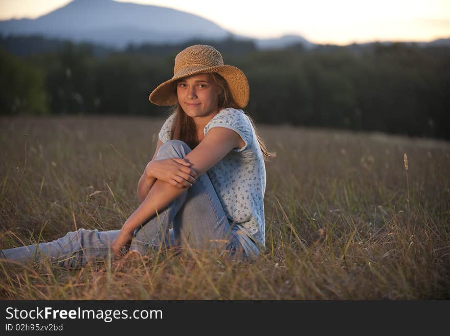 Pretty teen girl sitting in a field in the evening light. Pretty teen girl sitting in a field in the evening light