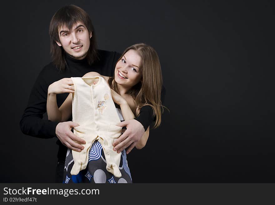 Pregnant couple embrace holding baby clothes. Pregnant couple embrace holding baby clothes