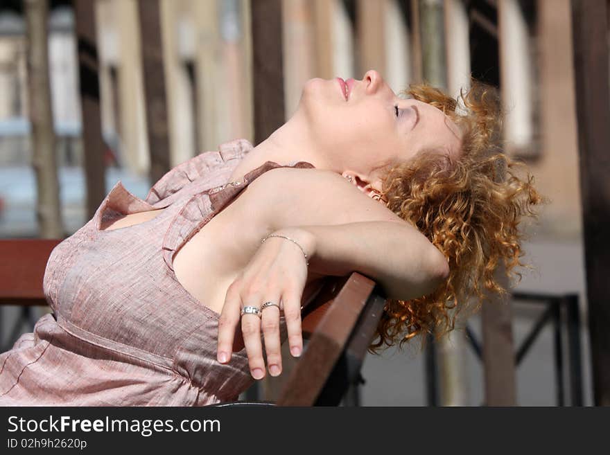 Red hair woman enjoying sun on bench in city in summer