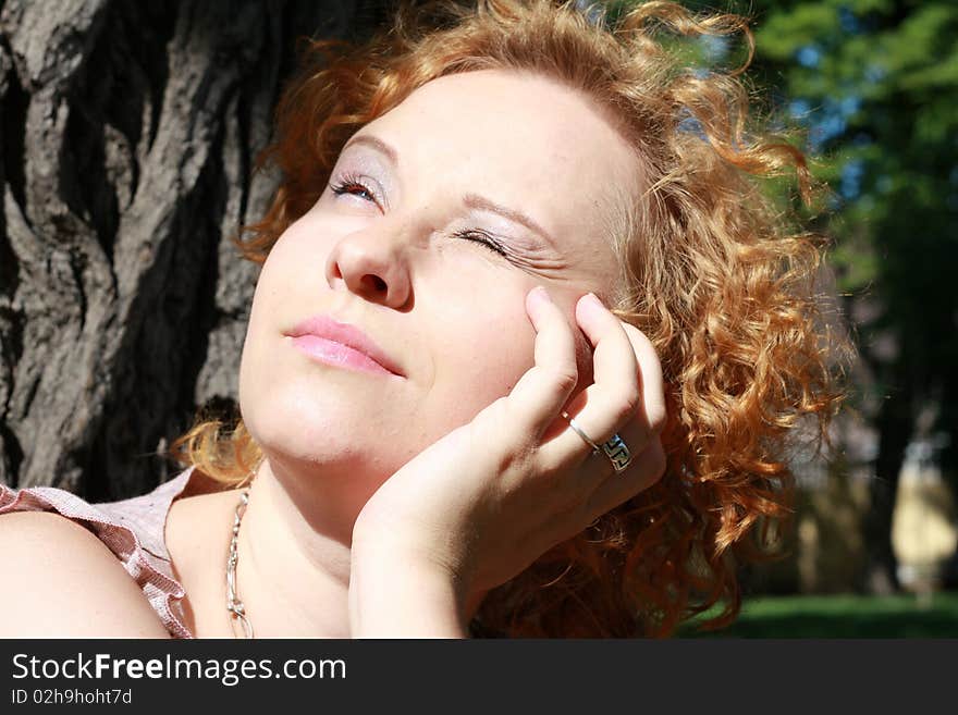 Portrait of the red hair girl near the tree in a park