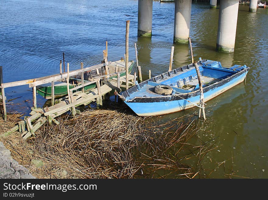 Little wooden blue boat anchored under a bridge